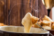 Close up, macro. Traditional french cheese fondue. Crouton dipped into stemy-hot cheese fondue on a long-stemmed fork. Copy space.