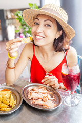 Wall Mural - Happy Asian woman in hat eating local Spanish cuisine grilled seafood and prawns