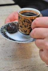 Close-up of hands holding a traditional arabic coffee served in a decorative black cup with gold ornaments