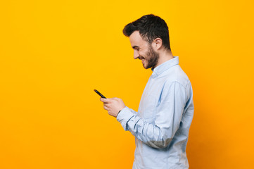 Young man smiling and using smartphone over yellow background