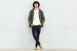 © sementsova321 - Full length shot of attractive self confident curly man dressed in green anorak, keeps both hands in pockets, enjoys spare time, isolated over white studio wall. People, youth and fashion concept