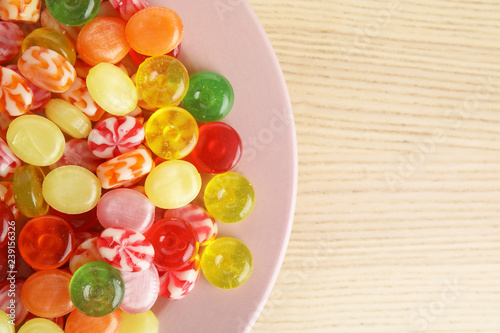 Plakat Plate with delicious colorful candies on wooden table, top view. Space for text
