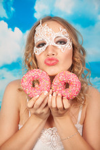 Cute Girl In White Lace Lingerie Indulges With Pink Glazed Donuts And Stands On A Blue Background Of Clouds