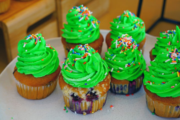 Wall Mural - Platter of blueberry cupcakes with green buttercream frosting and colorful sprinkles like a Christmas tree