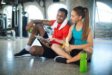 Young Active Man And Woman Having Snack At Break Between Workouts And Watching Online Videos In Tablet