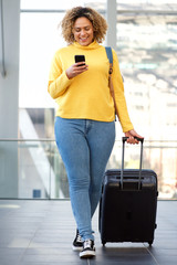 curvy african american woman walking with suitcase and mobile phone
