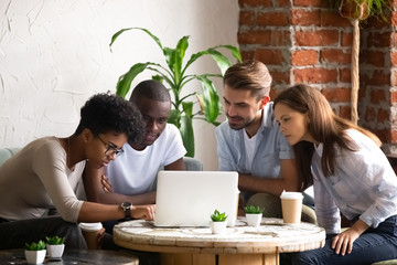 Focused African American woman with friends using laptop in cafe during lunch, watching movie, video online, black female showing colleagues photos, computer apps, checking social networks