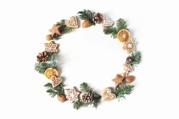 Wall Mural - Christmas circle floral composition. Wreath of fir tree branches, pine cones, gingerbread cookies and dry orange slices on white background. Winter holiday design. Flat lay, top view.