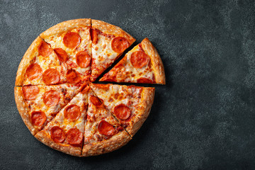 Wall Mural - Tasty pepperoni pizza and cooking ingredients tomatoes basil on black concrete background. Top view of hot pepperoni pizza. With copy space for text. Flat lay