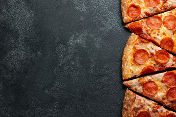 Wall Mural - Cut into slices delicious fresh pizza with sausage pepperoni and cheese on a dark background. Top view with copy space for text. Pizza on the black concrete table. flat lay