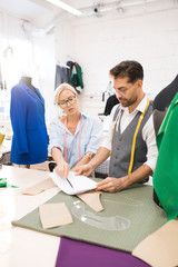 Wall Mural - High angle portrait of two fashion designers discussing sketches while making patterns at work in atelier studio