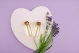 Fototapeta Lawenda - Lavender essential oil set in glass bottles and lavender flowers on pink heart on pastel lilac background.Organic Natural  Oil