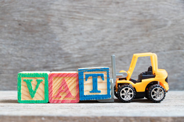 Sticker - Toy forklift hold color letter block T to complete word VAT (Abberviation of Value added tax) on wood background