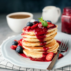 Wall Mural - Stack of pancakes with berry sauce, blueberry, strawberry and cranberry. Cup of coffee and cream on background. Square crop