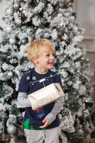 Little Boy With Blond Hair Smiles On A Christmas Tree Background