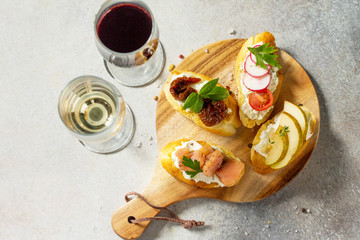 Italian Antipasti snacks set for Wine. Brushetta with Soft Cheese, Pear, Radish, Salmon and Dried Tomatoes on a light stone background. Top view flat lay background.