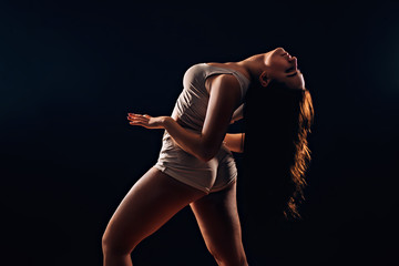 Sexy brunette woman with long hair dancing on black background in darkness