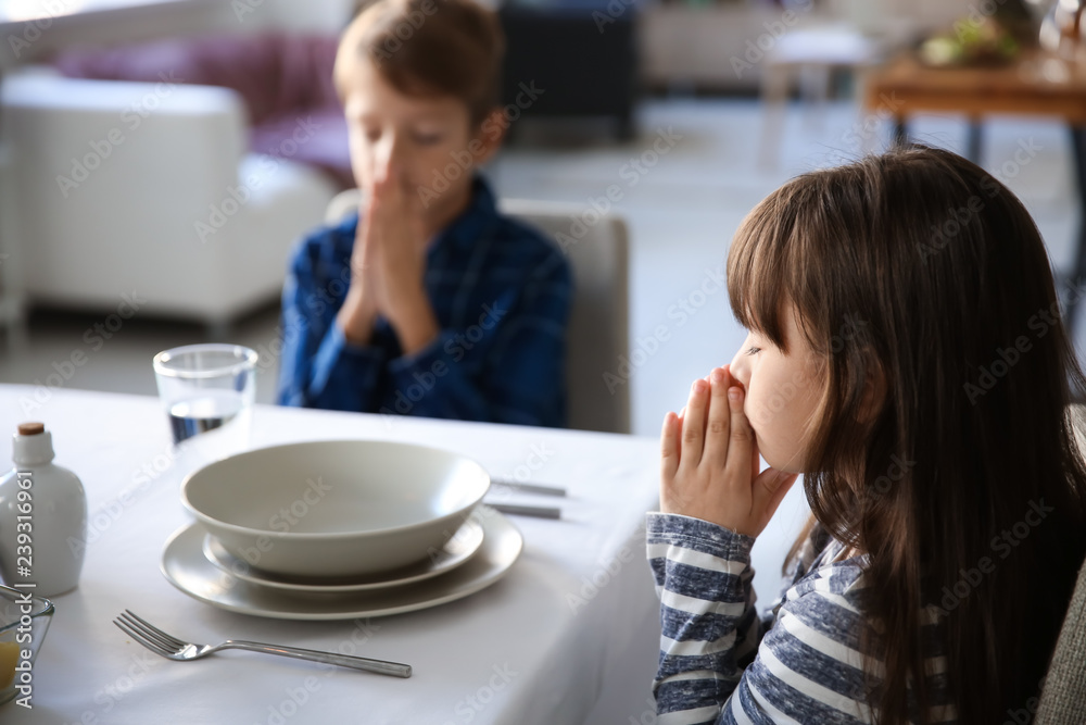 Cute children praying before meal at home