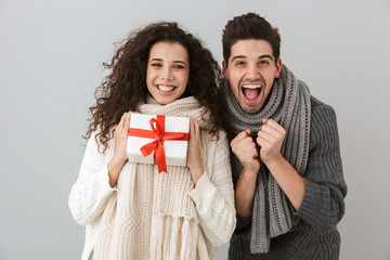 Sticker - Image of european man and woman rejoicing while standing with present box, isolated over gray background