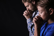 Praying father and son on dark background