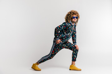 Wall Mural - Adult positive smiling funky man with curly hair style in suglasses and vintage clothes posing on white studio background. Funny portrait of stylish male person. 80s fashion. Unusual eccentric guy.