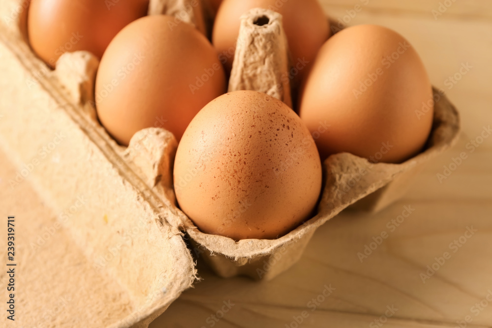 Carton box with raw chicken eggs on wooden table
