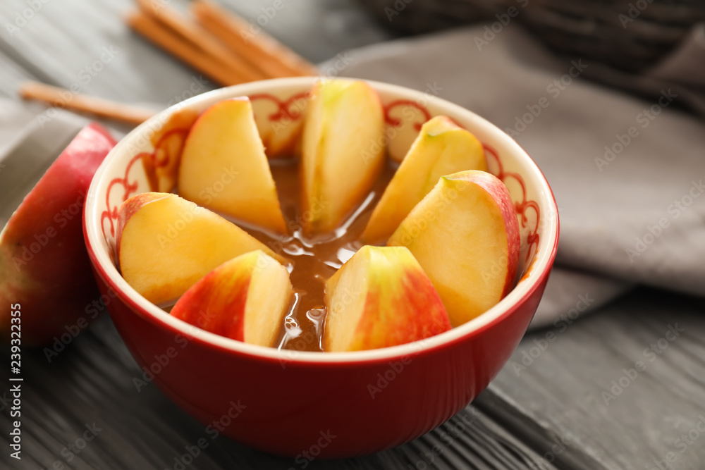 Apple wedges in bowl with sauce on wooden table