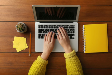 Young woman using laptop on wooden table, top view