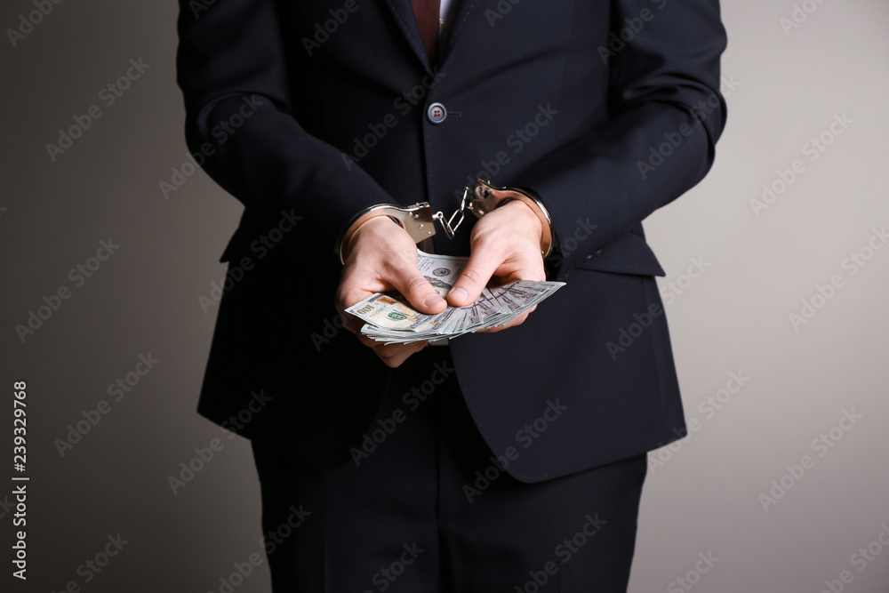 Businessman in handcuffs with bribe on grey background. Corruption concept