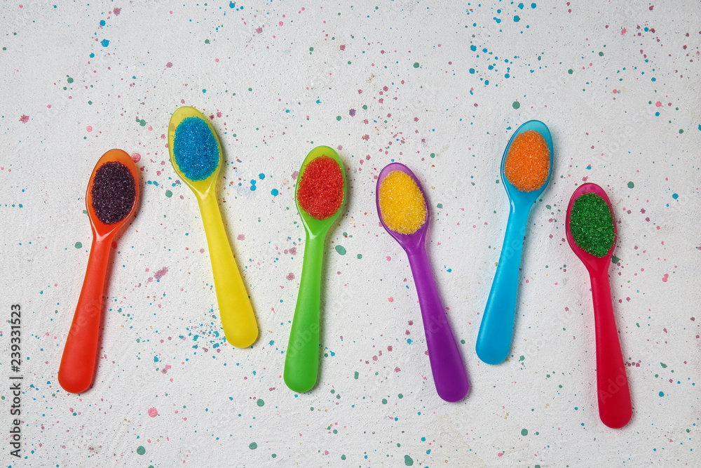 Spoons with color sugar on light background