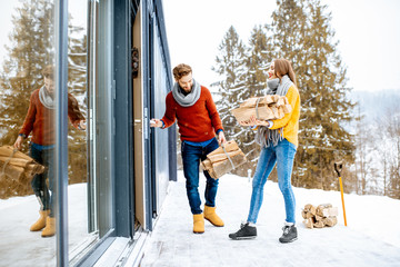 Young lovely couple dressed in colorful sweaters entering their modern home with firewoods in the mountains during the winter