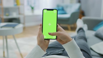 Woman at Home Lying on a Couch using Smartphone with Green Mock-up Screen, Doing Swiping, Scrolling Gestures. Girl Using Mobile Phone, Internet Social Networks Browsing. Point of View Camera Shot.