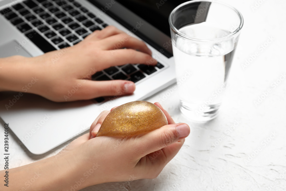Woman squeezing stress ball while working with laptop