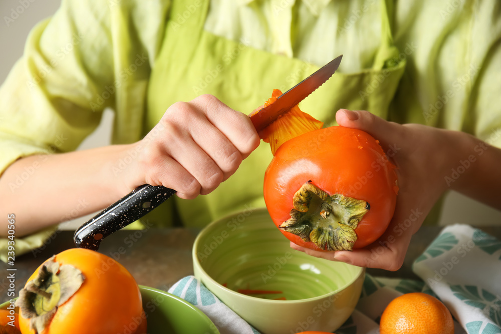 Woman peeling ripe persimmon at table