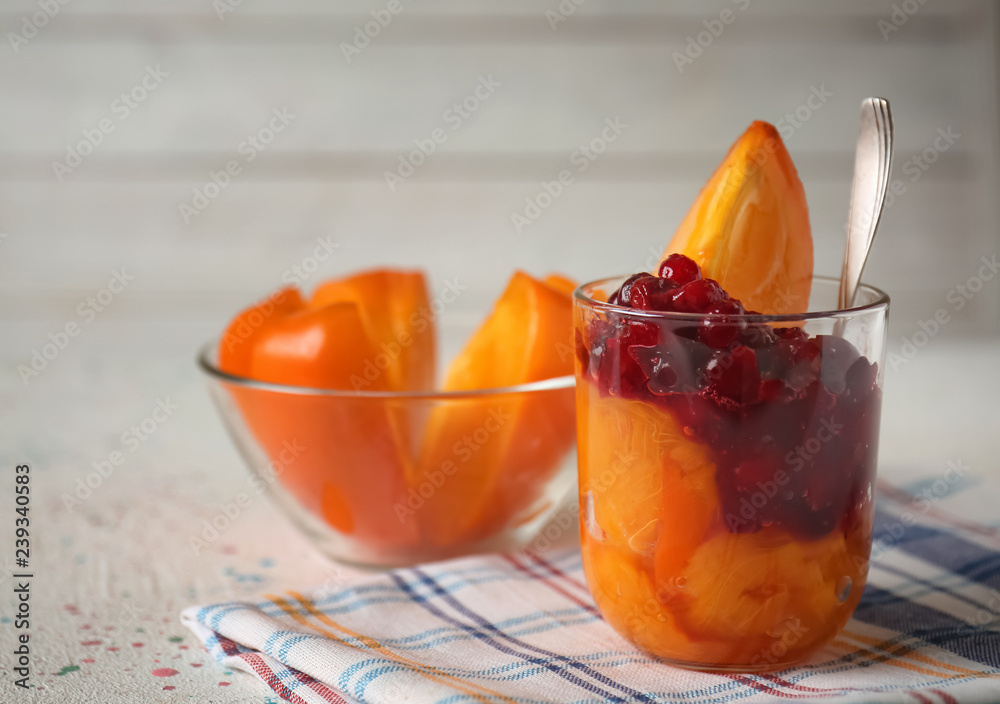 Glass with tasty ripe persimmons and berries on table