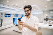 © Dusan Petkovic - Smiling man standing in tech store with smart phone in his hands. New technologies concept.
