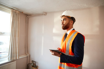 Surveyor In Hard Hat And High Visibility Jacket With Digital Tablet Carrying Out House Inspection