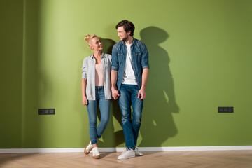 smiling couple holding hands, standing by green wall and looking at each other