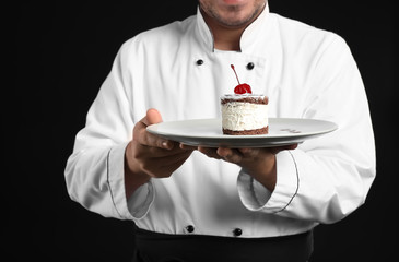 Male chef with tasty dessert on dark background, closeup