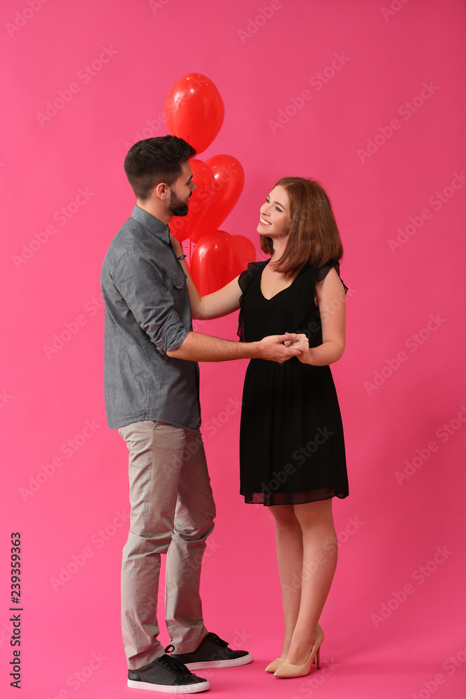 Loving young couple with heart-shaped balloons on color background. Celebration of Saint Valentine's Day