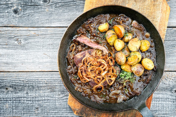 Traditional dry aged sliced roast beef with fried onion rings and potato chips as closeup in a wrough-iron pan with brown sauce