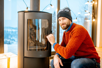 Portrait of a handsome man in sweater near the fireplace in the modern house during the winter time