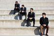 © Erickson Stock - Four businessmen sitting on steps outside a building.
