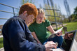 © Erickson Stock - Teenage boy doing his homework outdoors on his laptop with the help of his girlfriend.