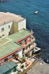 Mediterranean style multi story terrace house with flat roofs on steep rocky cliff right above sea surface.