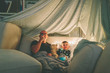 A father and son watching a movie in a fort and eating popcorn. 
