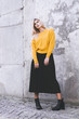 © HELP PEOPLE UKRAINE - Fashionable girl. A girl in a yellow sweater, wearing a black skirt and boots in the background of a concrete wall. Clothes in style oversize
