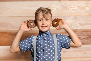 Poster - Cute little boy with donuts on wooden background