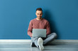 © Pixel-Shot - Young man with laptop sitting near color wall