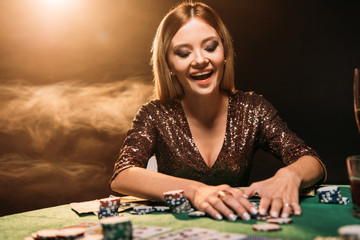 happy attractive girl taking poker chips and looking down at casino